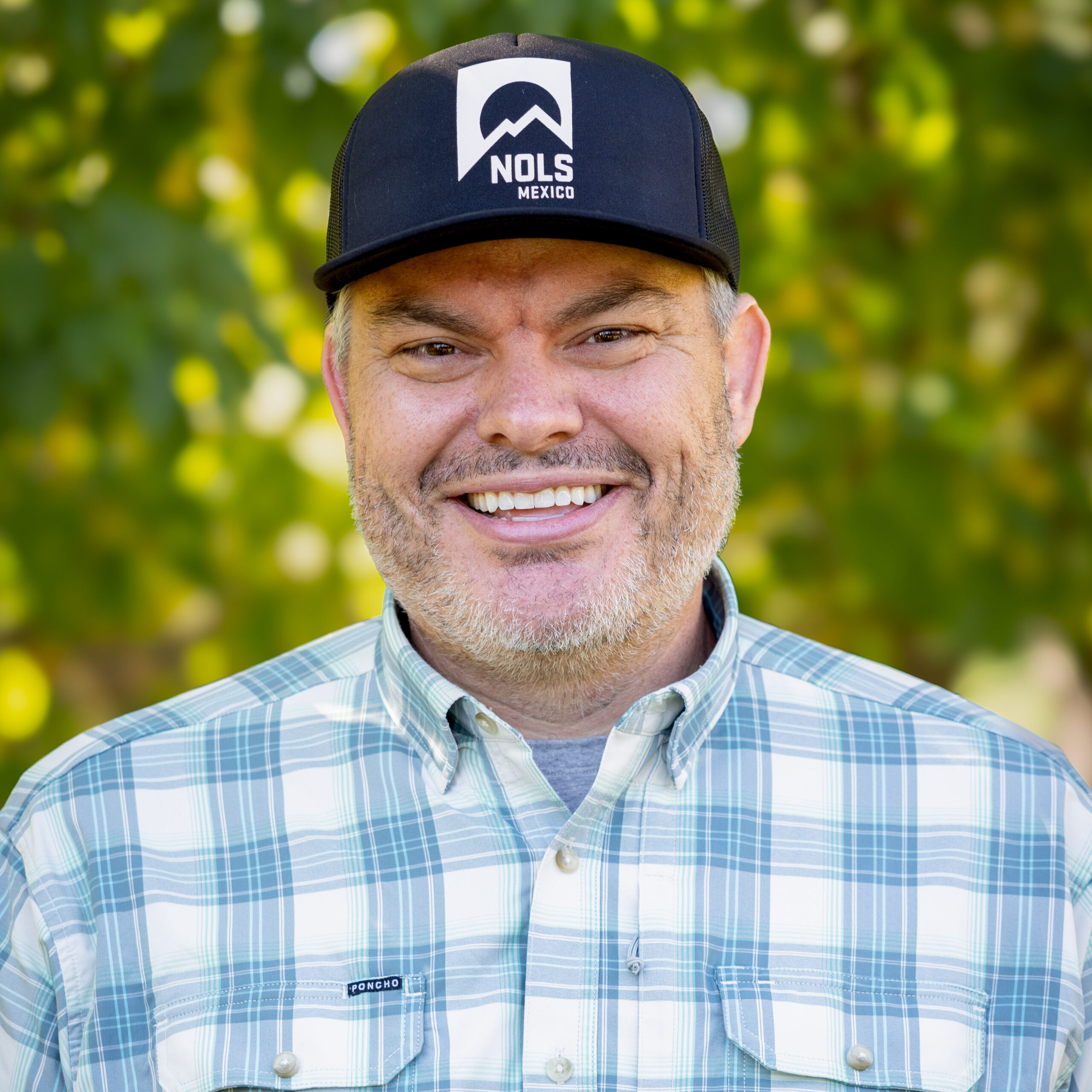A man with a black hat sporting a NOLS logo smiles for the camera