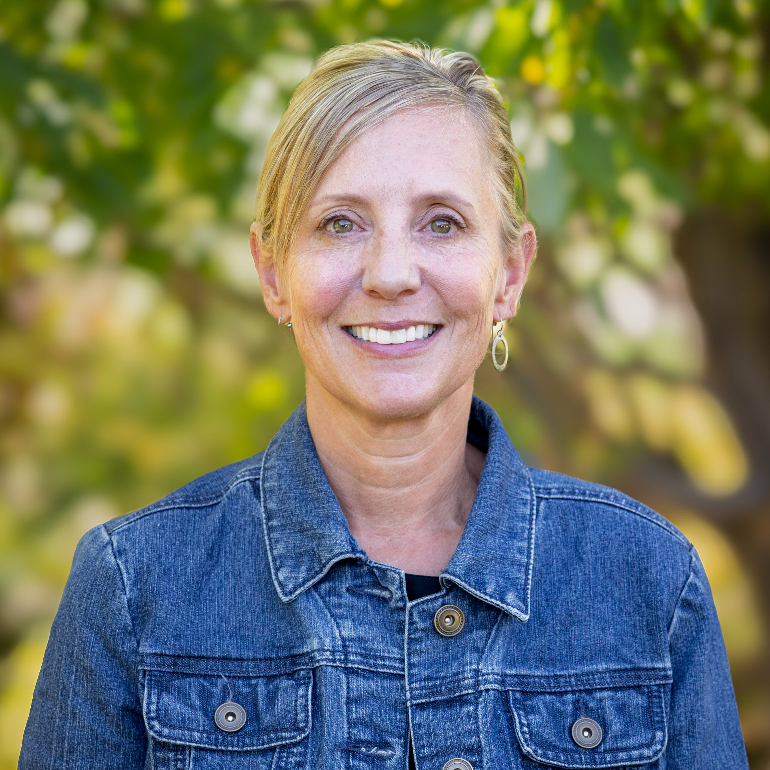 Jayme_Blackburn_headshot_2025 A woman with blond hair is wearing a jean jacket and smiling at the camera